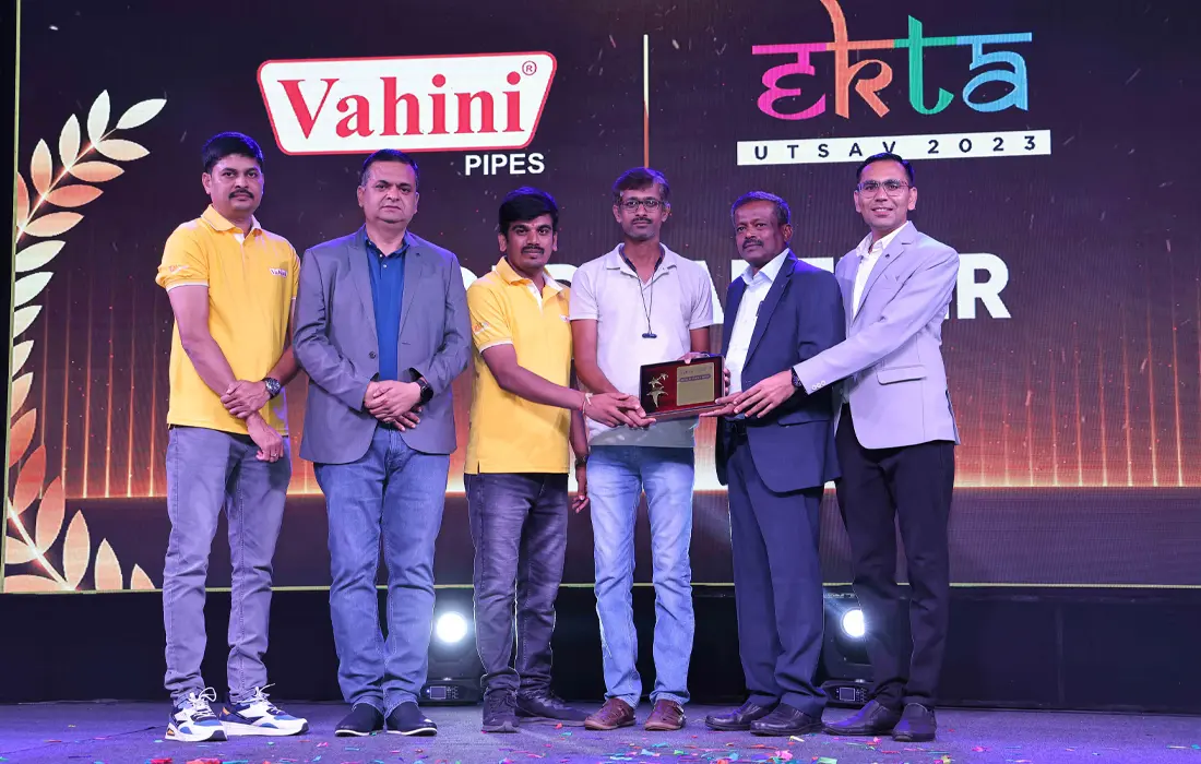 An award being presented on stage in front of Vahini and Ekta Utsav 2023 backdrops.