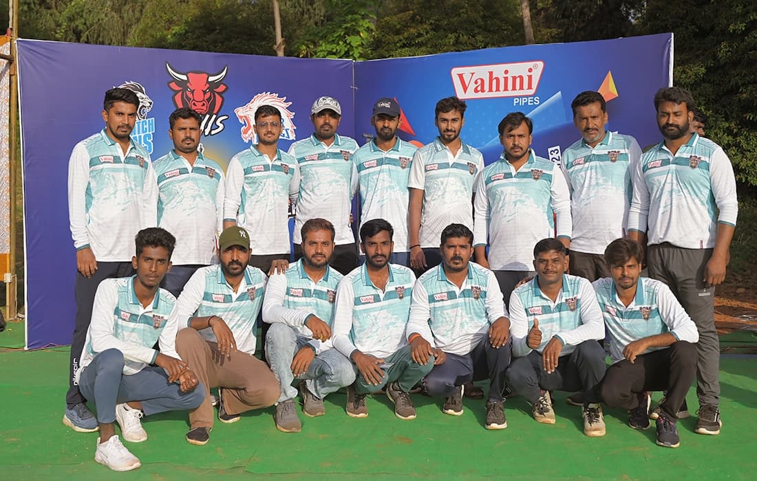A cricket team in matching jerseys posing in two rows in front of a Vahini banner.