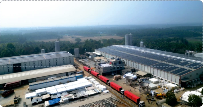 Aerial view of the Vahini campus in Tumakuru: production sheds with solar panels on the roof, silos, finished pipe stacked in the yard and red trucks loading