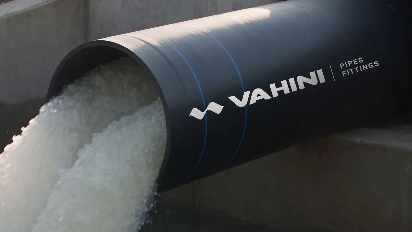 A large black pipe carrying the Vahini Pipes and Fittings name, water pouring from its mouth in full flow.