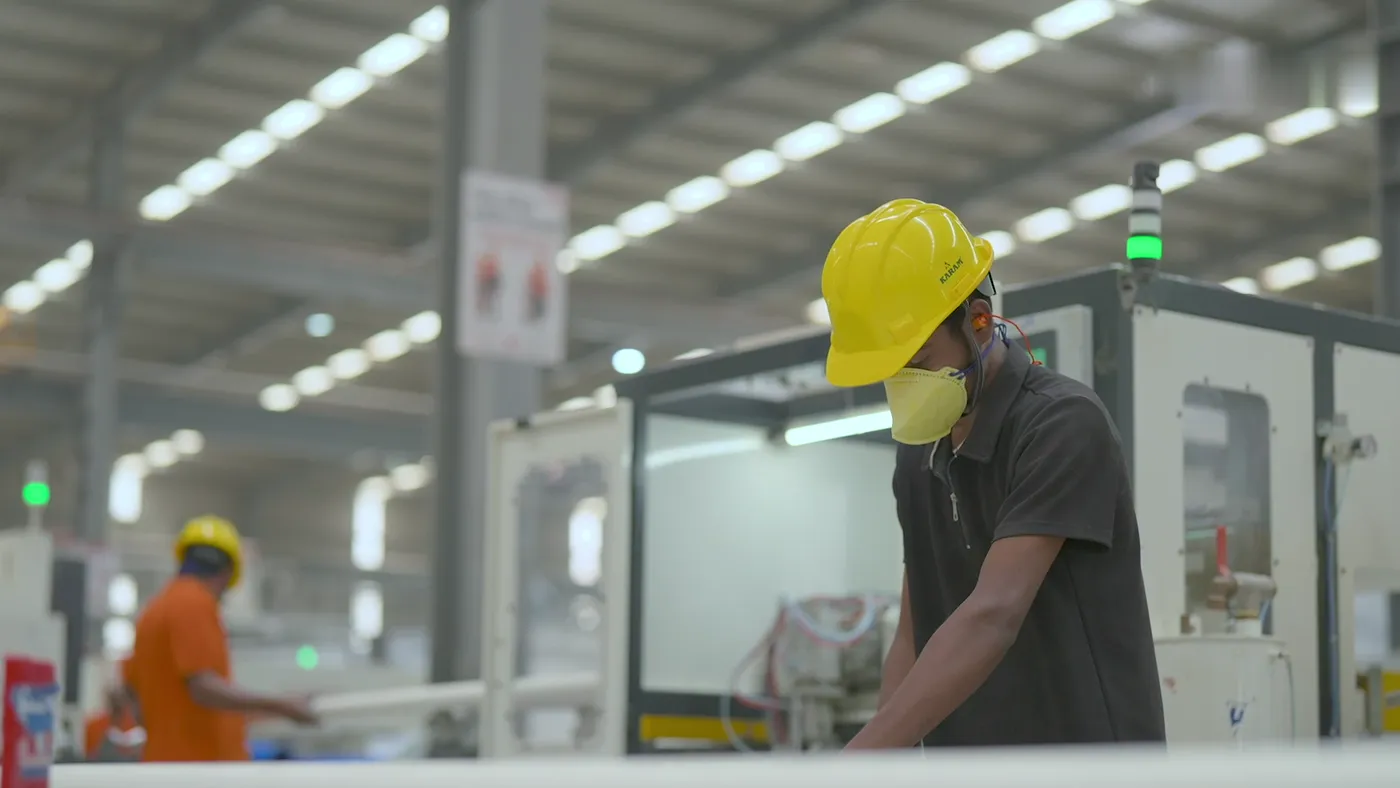 A worker in a yellow hard hat and mask at a machine on the production line.