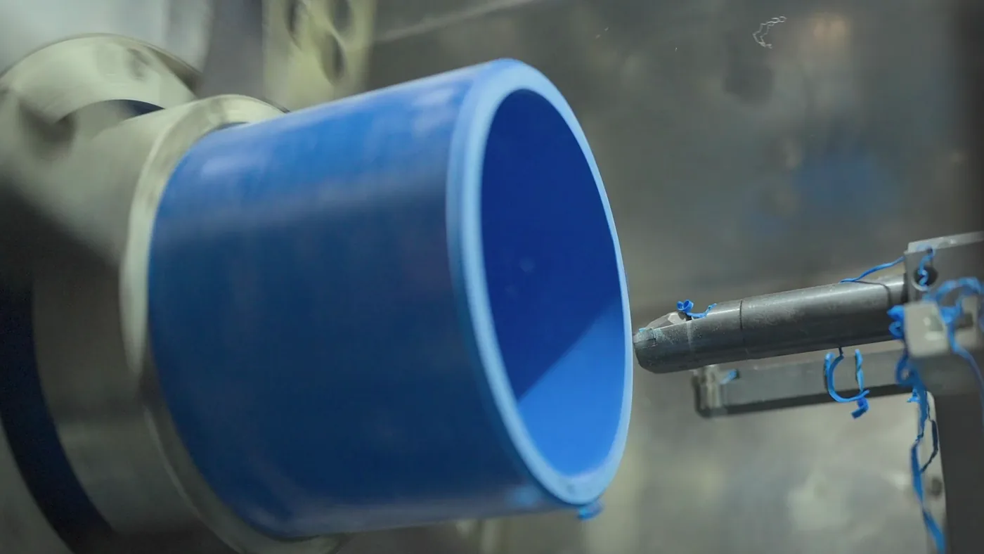 The end of a blue pipe held in a machine, a cutting tool at its edge.